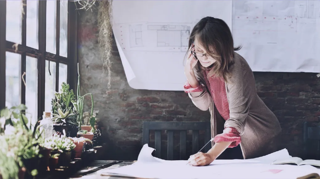 An architect in glasses leaning over building blueprints at a studio desk