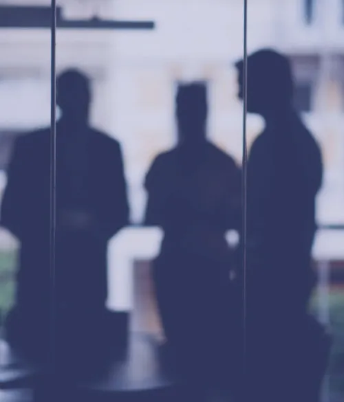 Silhouettes of three people in conversation behind a glass partition