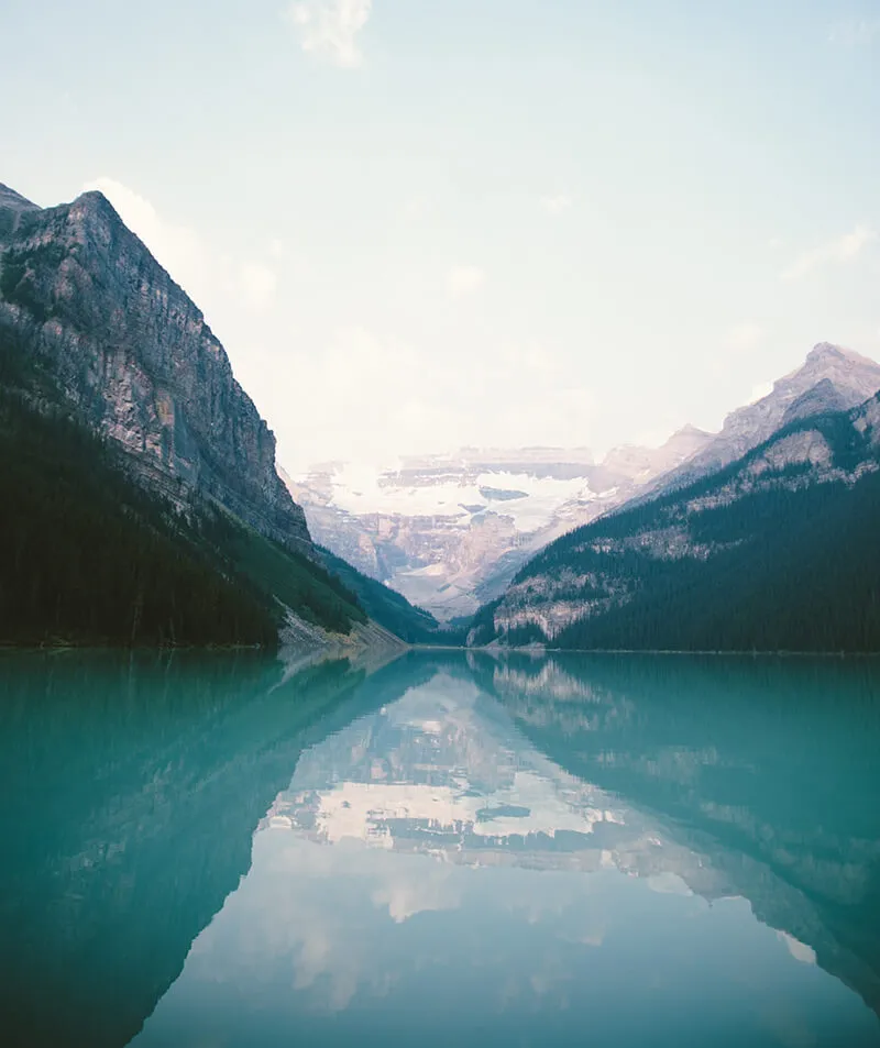 A still mountain lake mirroring snow-capped peaks and forested slopes