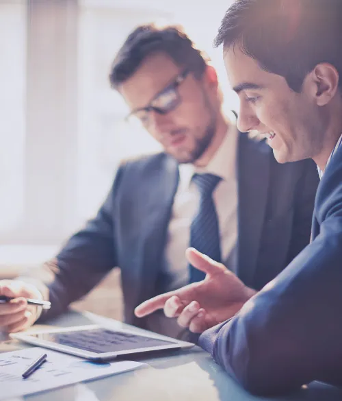 Two businessmen in suits reviewing documents and a tablet together
